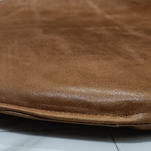 May include: A brown leather chair cushion with a rounded shape and a stitched edge.