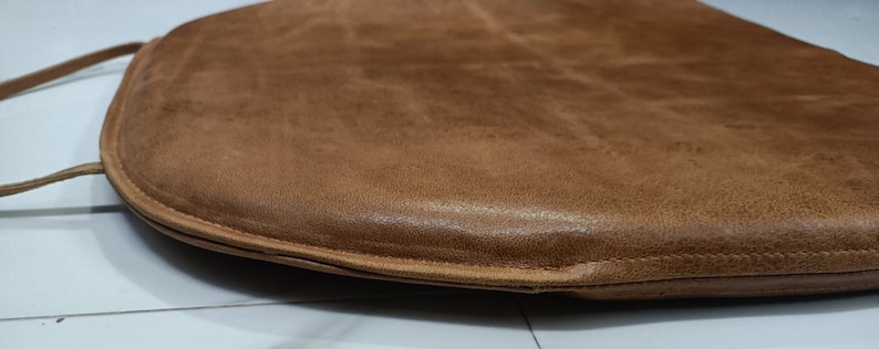 May include: A brown leather chair cushion with a rounded shape and a stitched edge.