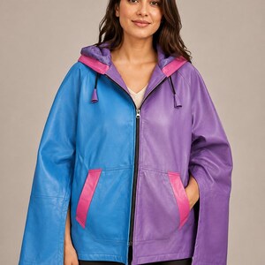 May include: A color-blocked hooded jacket featuring a bright blue right side and a purple left side. The garment includes a central black zipper, two front pockets with pink trim, and wide, open-style sleeves. The hood interior is purple.