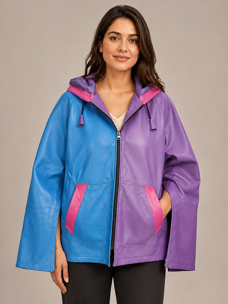 May include: A color-blocked hooded jacket featuring a bright blue right side and a purple left side. The garment includes a central black zipper, two front pockets with pink trim, and wide, open-style sleeves. The hood interior is purple.