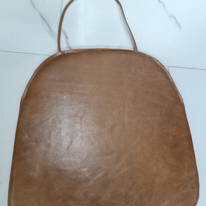 May include: A brown leather chair cushion with a tie string. The cushion is round and has a smooth surface.