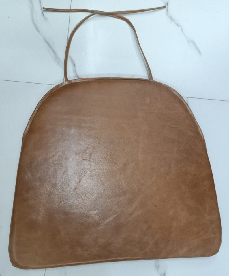 May include: A brown leather chair cushion with a tie string. The cushion is round and has a smooth surface.