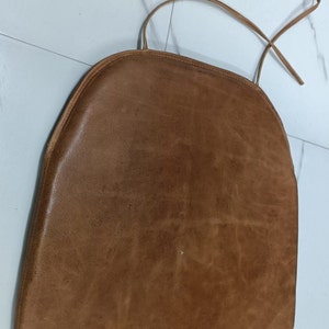 May include: A brown leather chair cushion with a tie closure.