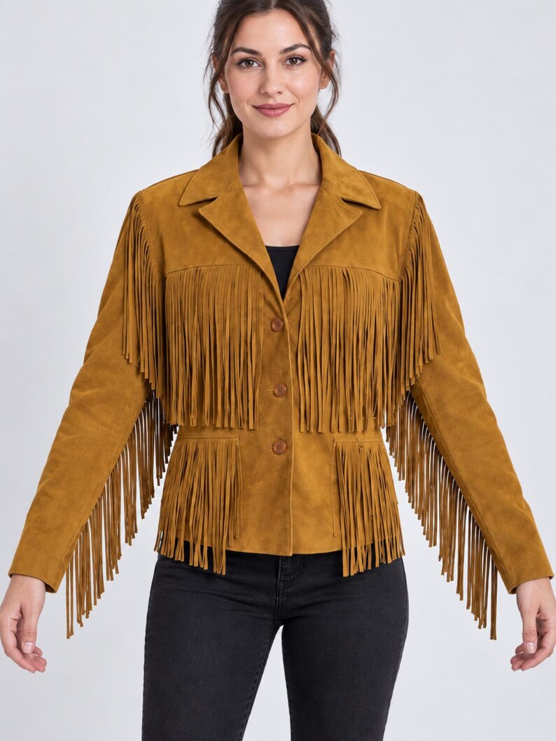 K&ouml;nnte beinhalten: Eine senfgelbe Wildlederjacke mit langen Fransen an Brust, &Auml;rmeln und unterem Saum. Die Jacke hat einen klassischen Kragen, eine Knopfleiste mit drei Kn&ouml;pfen und lange &Auml;rmel. Sie wird mit einer schwarzen Jeans kombiniert.