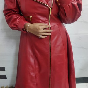 May include: A long, red coat featuring a notched lapel, gold-tone metal zippers, and puffed sleeves. The coat has a full-length front zipper closure, a fitted waist, and a flared skirt silhouette, constructed with smooth, solid-colored material.
