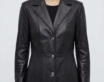 May include: A black leather coat featuring a notched lapel collar, long sleeves, and a front button closure with four silver-toned buttons. The coat has a tailored fit with visible vertical seam detailing along the front and a smooth finish.