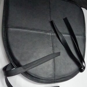 May include: Black leather seat cushion with straps. The cushion is divided into four sections with stitched seams. The straps are long and thin, designed for securing the cushion.