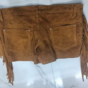 K&ouml;nnte beinhalten: Braune Wildleder-Shorts mit Fransenbesatz. Die Shorts haben zwei Taschen auf der R&uuml;ckseite und einen Knopf- und Rei&szlig;verschluss.