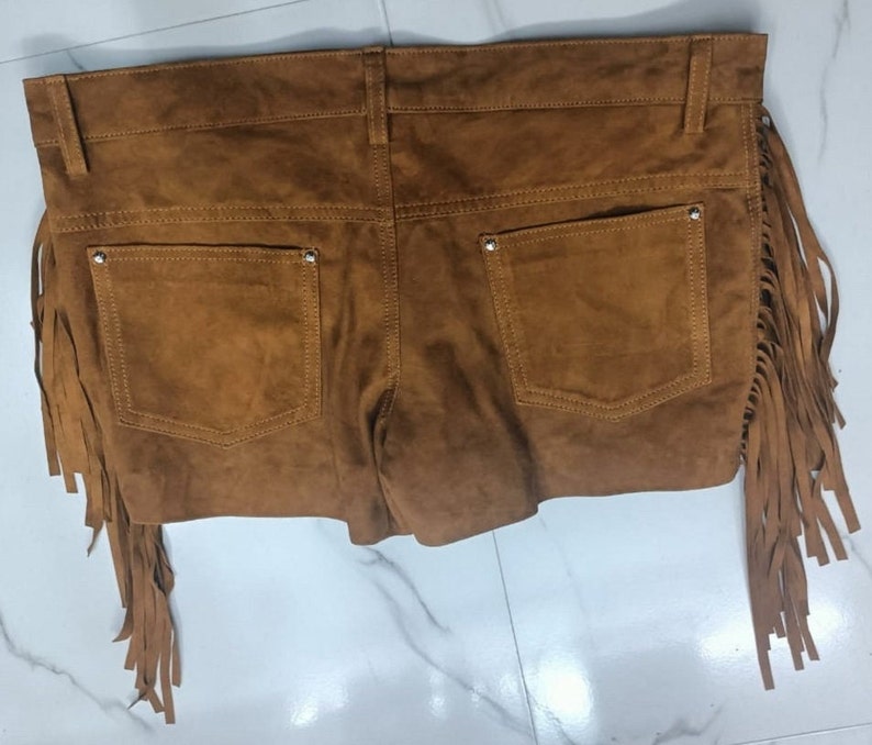 K&ouml;nnte beinhalten: Braune Wildleder-Shorts mit Fransenbesatz. Die Shorts haben zwei Taschen auf der R&uuml;ckseite und einen Knopf- und Rei&szlig;verschluss.