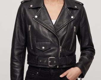 May include: A black leather motorcycle jacket featuring a wide notched collar with silver-tone metal snaps, an asymmetrical front zipper closure, two vertical zippered chest pockets, a small flap pocket with a snap, and a matching buckled waist belt.