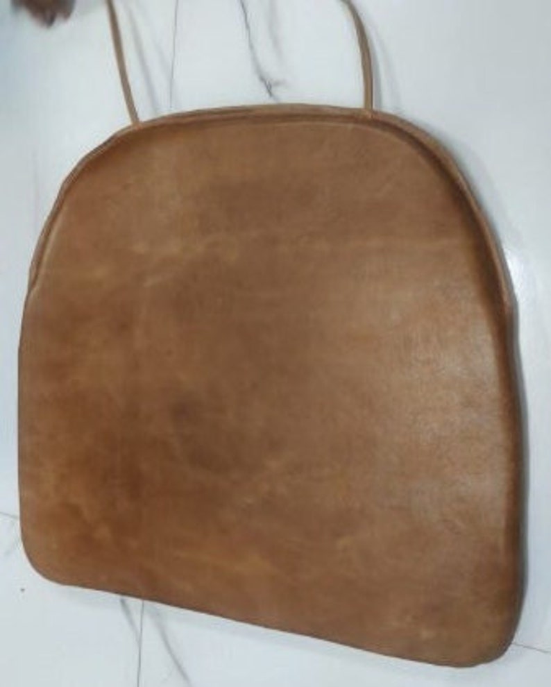 May include: A brown leather chair cushion with a rounded shape and a simple design.