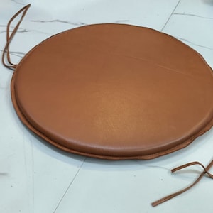 May include: A round brown leather chair cushion with ties.