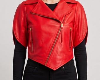 May include: A bright red leather jacket featuring short, wide sleeves, a wide notched collar, and an asymmetrical front zipper closure. The jacket includes two vertical zippered pockets on the front, all finished with gold-toned metal hardware.