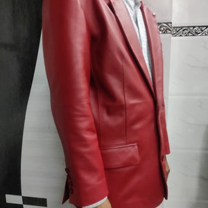 Może przedstawiać: Żywy czerwony sk&oacute;rzany blazer z klasycznym zapięciem na dwa guziki i klapami z wycięciami. Blazer posiada kieszeń na piersi i dwie kieszenie z klapkami. Rękawy mają mankiety zapinane na guziki. Blazer jest noszony na białej i niebieskiej koszuli w paski.