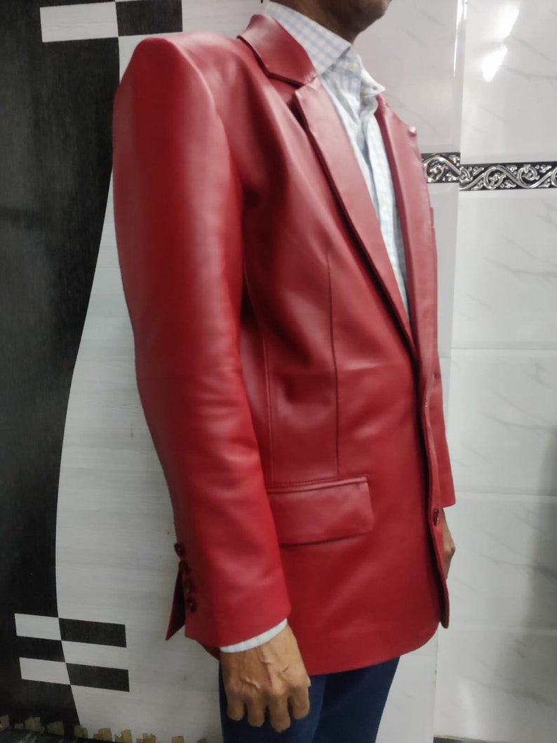 Może przedstawiać: Żywy czerwony sk&oacute;rzany blazer z klasycznym zapięciem na dwa guziki i klapami z wycięciami. Blazer posiada kieszeń na piersi i dwie kieszenie z klapkami. Rękawy mają mankiety zapinane na guziki. Blazer jest noszony na białej i niebieskiej koszuli w paski.