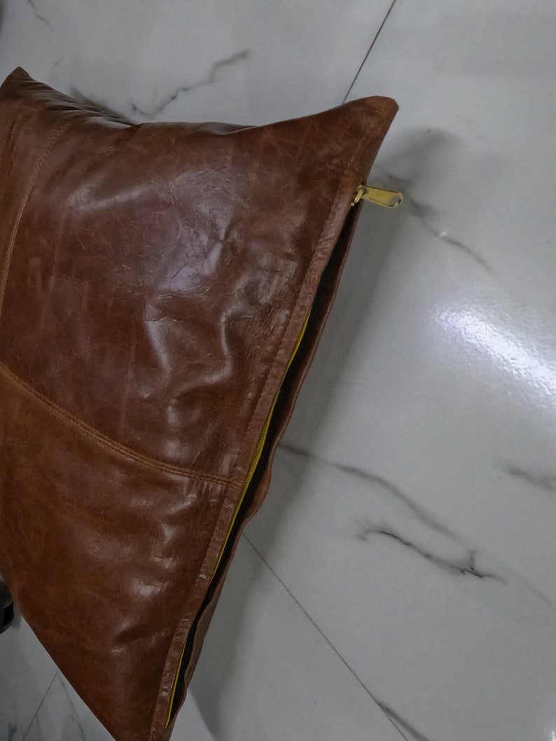 May include: A brown leather cushion with a yellow zipper. The cushion is made from soft, supple leather and has a smooth, even texture.