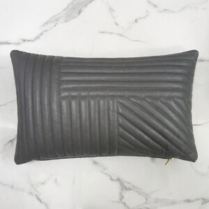 May include: A rectangular charcoal gray pillow featuring a quilted pattern with vertical, horizontal, and diagonal stitched lines. The pillow has a smooth texture and includes a small gold-toned metal zipper pull visible on the bottom right corner.