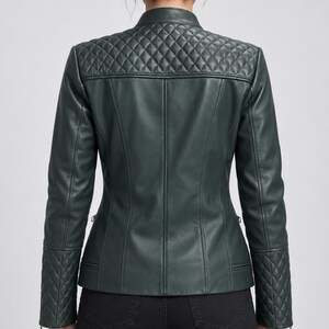 May include: A dark forest green jacket featuring a mandarin collar, long sleeves, and a quilted diamond pattern on the upper back shoulders and lower sleeves. The jacket has a smooth finish on the main body panels and vertical seam detailing.