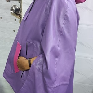 May include: A lavender leather hooded jacket featuring a vibrant magenta hood lining and a matching magenta pocket trim. The jacket has wide sleeves, a smooth finish, and a black drawstring cord at the neck, providing a distinct color-blocked appearance.