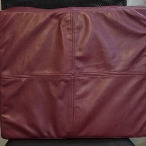 May include: A burgundy leather cushion with a square shape and four stitched panels.