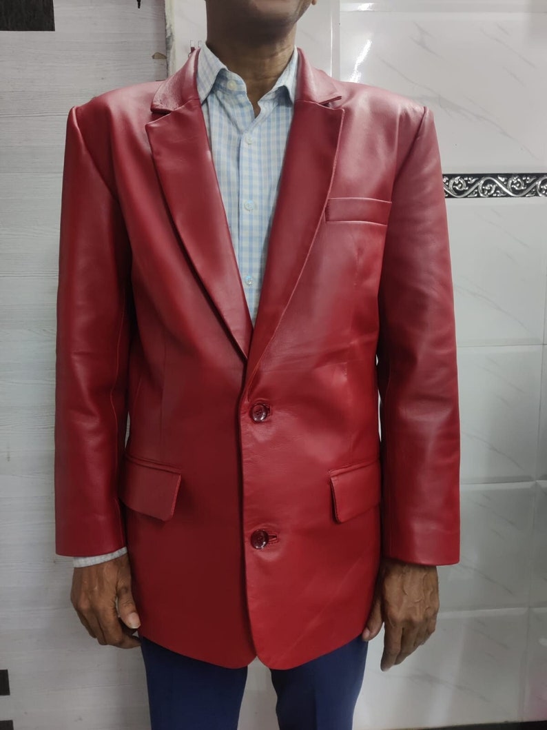 Może przedstawiać: Żywy czerwony sk&oacute;rzany blazer z klasycznym zapięciem na dwa guziki i klapami z wycięciami. Blazer posiada dwie przednie kieszenie i kieszeń na piersi. Osoba ma na sobie jasnoniebieską i białą koszulę w kratę. Blazer jest połączony z niebieskimi spodniami.