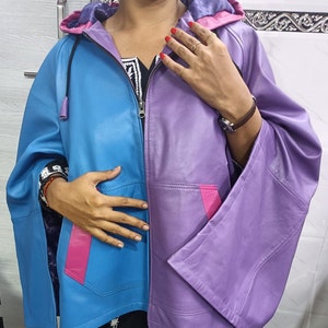 May include: A color-blocked hooded jacket featuring a bright blue right side and a purple left side. The jacket includes a front zipper, wide sleeves, and two front pockets accented with vibrant pink trim. The hood interior is lined in purple.