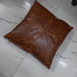 May include: A brown leather square cushion with a zip closure.