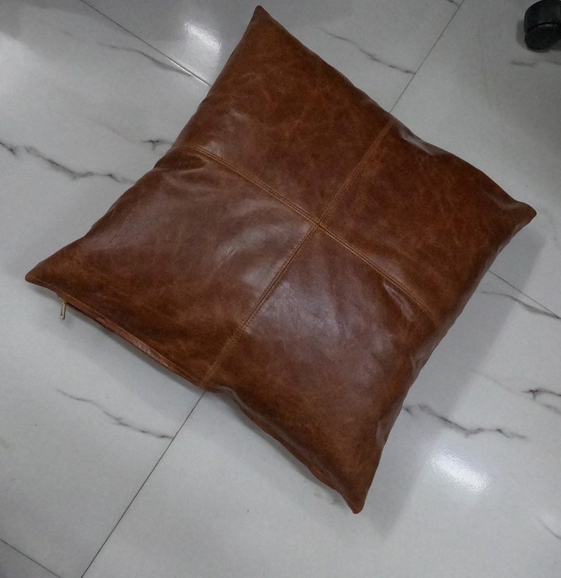 May include: A brown leather square cushion with a zip closure.