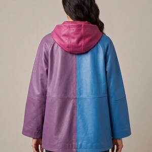 May include: A color-blocked leather jacket featuring a purple left side and a blue right side. The jacket includes a magenta hood, long sleeves, and a horizontal seam across the midsection. The design is symmetrical with a smooth finish.
