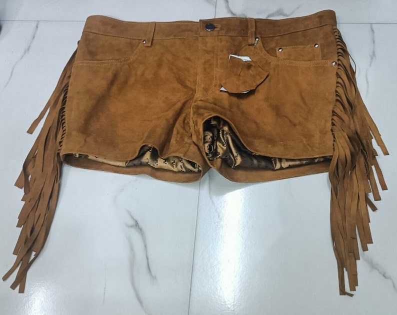 K&ouml;nnte beinhalten: Braune Wildleder-Shorts mit Fransen-Details. Die Shorts haben ein F&uuml;nf-Taschen-Design und einen Knopf- und Rei&szlig;verschluss.