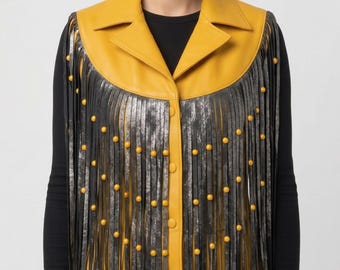 May include: A sleeveless vest featuring a mustard yellow collar and front panel with a button-down closure. The garment is adorned with long, metallic silver fringe strips that hang from the shoulders and chest, accented by small yellow studs.