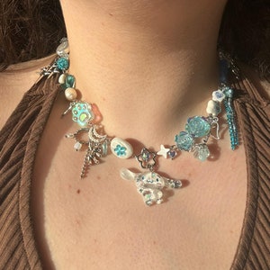 Könnte beinhalten: Eine weiße und blaue Glücksbringerkette mit einer Vielzahl von Anhängern, darunter Blumen, Sterne und eine kleine weiße Tierfigur. Die Kette besteht aus einer silbernen Kette und hat einen blauen und weißen Perlenabschnitt.
