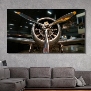 May include: A close-up view of the front of a vintage aircraft propeller. The propeller is silver with yellow tips and is set against a dark background.