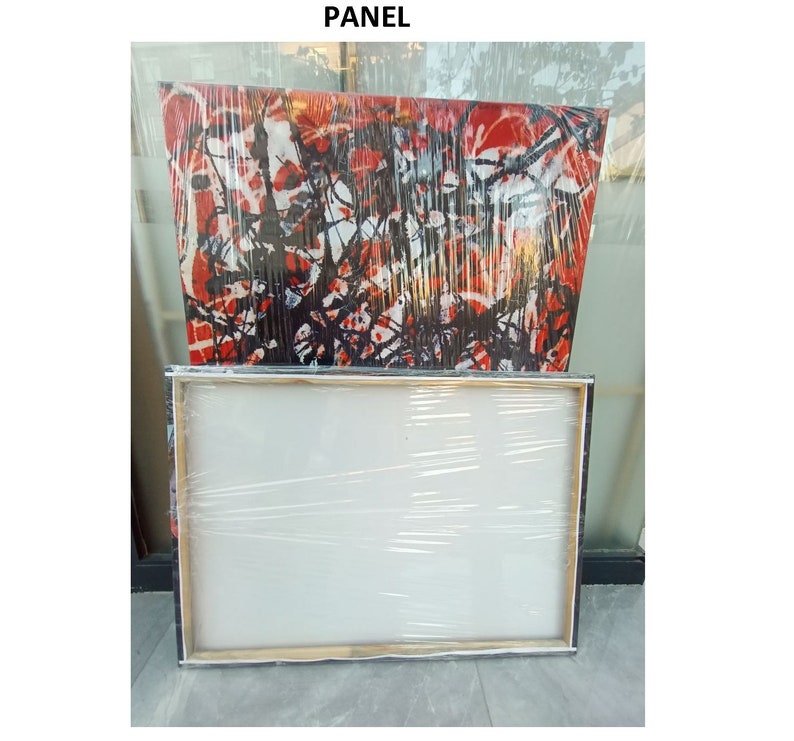 May include: A white canvas panel wrapped in plastic, ready for painting. The panel is sitting on top of a larger canvas with an abstract painting of black and red lines.