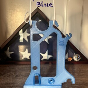 Puede incluir: Un soporte impreso en 3D de color azul claro con un asa blanca, que presenta varios recortes y una base plana. El texto "Transparent Light Blue" est&aacute; impreso sobre el objeto. La estructura incluye un marco vertical con varias muescas.