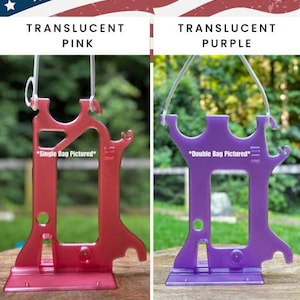 Side-by-side comparison of two Hero Tubie™ pump stands for the Kangaroo™ Omni. The left shows the stand in translucent pink labeled “Single Bag Pictured.” The right shows the stand in translucent purple labeled “Double Bag Pictured,” though this listing is for single bag use only. Both stands feature a lightweight, 3D-printed design with detachable hangers and are displayed outdoors on wooden surfaces with blurred green backgrounds. Text at the bottom reads “Kangaroo OMNI Single Bag Hero Tubie.”