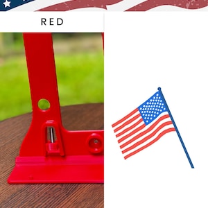 Patriotic-themed product photo featuring a Hero Tubie™ pump stand for the Kangaroo™ Omni in a bright “Red” color. The stand is lightweight, 3D-printed, and includes a detachable white hanger for holding a single feeding bag. It’s displayed on a wooden surface outdoors with blurred green grass and fencing in the background. To the right of the product is an illustrated American flag graphic. Text at the bottom reads “Kangaroo OMNI Single Bag Hero Tubie.”