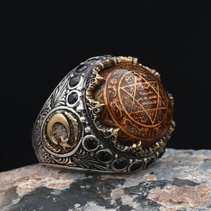 Könnte beinhalten: Ein silberner Ring mit einem schwarzen Onyxstein und einer goldfarbenen Mitte mit einem Davidstern und arabischer Schrift.