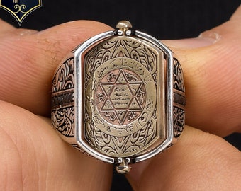 May include: A silver ring with a gold-toned center featuring a six-pointed star and Arabic script. The ring is detailed with intricate engravings and has a rotating design.