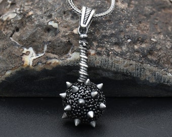 May include: A silver necklace with a black gemstone studded mace pendant. The pendant has a twisted silver chain and a round ball shape with spikes.