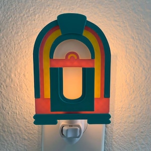 May include: A teal blue and red nightlight shaped like a vintage jukebox with yellow accents. The nightlight has a white light that shines through the front.