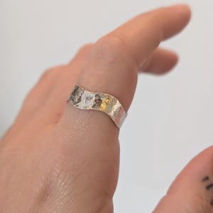 May include: A silver ring with a wavy, hammered design. The ring is worn on a finger.