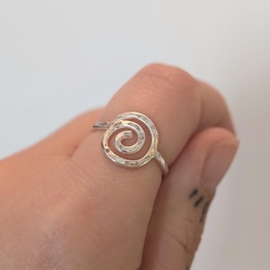 May include: A silver ring with a hammered finish and a spiral design.