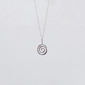 May include: A delicate silver necklace featuring a spiral pendant. The pendant is a small, open spiral design suspended from a fine chain. The necklace is displayed against a plain white background, highlighting its minimalist aesthetic.