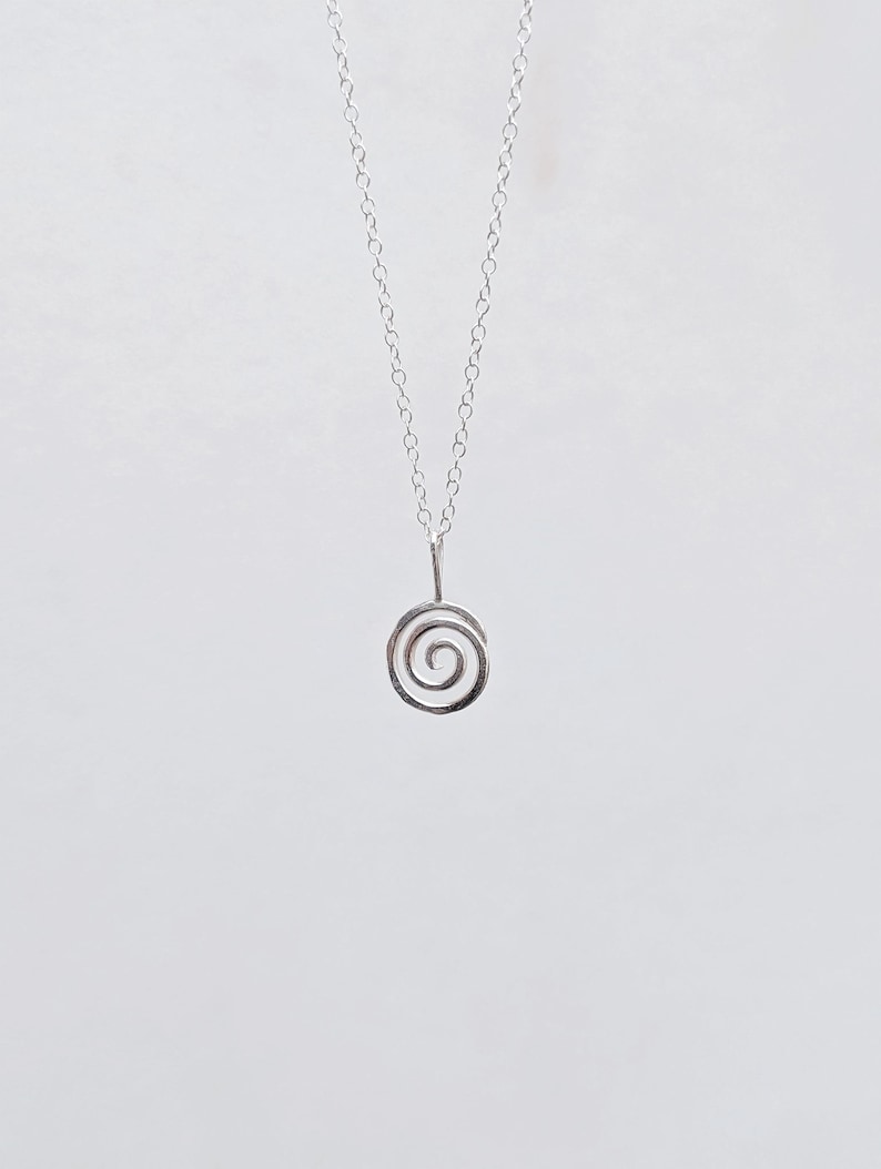May include: A delicate silver necklace featuring a spiral pendant. The pendant is a small, open spiral design suspended from a fine chain. The necklace is displayed against a plain white background, highlighting its minimalist aesthetic.