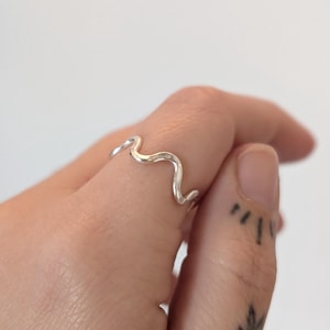 May include: A silver wavy ring worn on a finger.