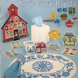 May include: A craft instruction booklet titled American School of Needlework Easy to Make Plastic Canvas Projects Volume I. The cover displays various plastic canvas items including a schoolhouse photo frame, a tissue box cover, and coasters.