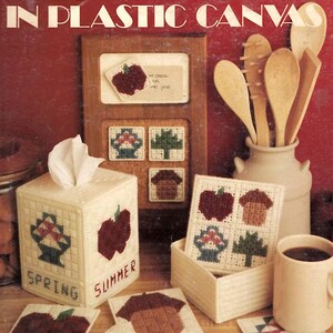May include: A craft instruction booklet titled Patchwork Seasons in Plastic Canvas by Teal Lee Elliott, featuring patterns for a tissue box cover, coasters, and wall decor with seasonal motifs like apples, acorns, and trees in cream plastic canvas.