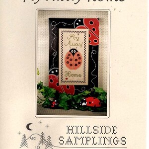 May include: A cross-stitch pattern titled "Fly Away Home" featuring a ladybug design. The image includes the text "Fly Away Home" and "Home". The design is framed with ladybug accents and greenery. The brand name "Hillside Samplings" is also visible.