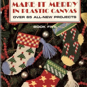 May include: A craft instruction booklet titled Make It Merry In Plastic Canvas Book Five, featuring three plastic canvas Christmas stockings with tree, candy cane, and star patterns, decorated with yarn tassels and festive colors.